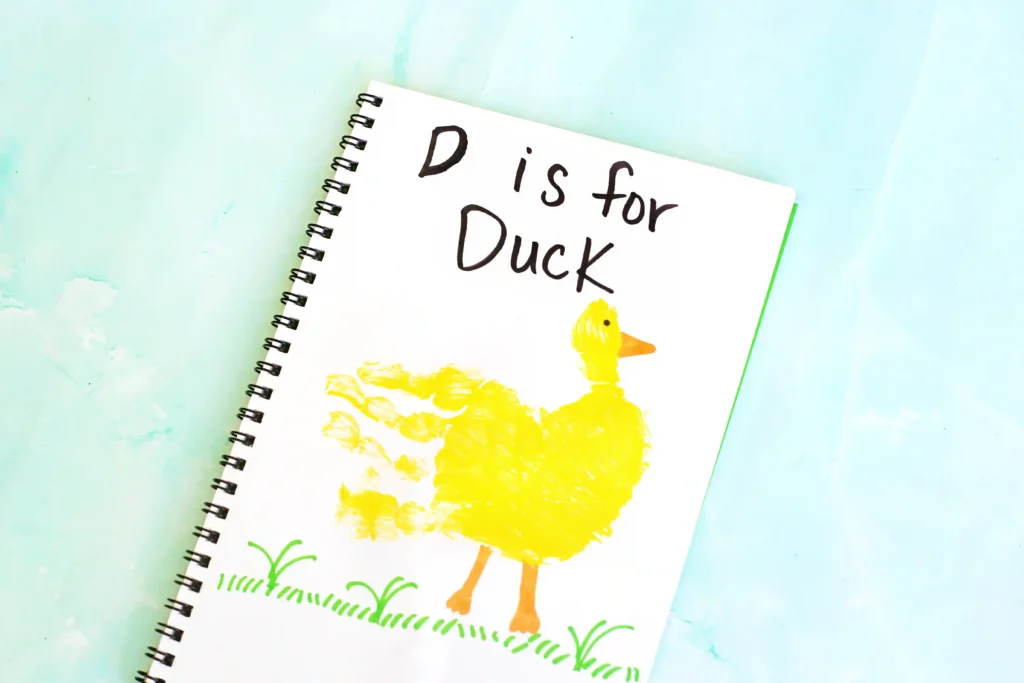 Letter D Duck Handprint Craft - Cultivating Brilliant Minds Notebook page with handwriting'D is for Duck' beside a yellow duck illustration on green grass and a turquoise background.