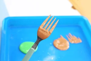 Brown paint on a fork over a bright blue surface behind it.
