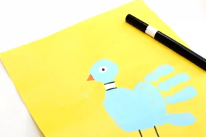 Yellow notebook with a blue bird drawing and blue clouds; a black marker rests on it diagonally.