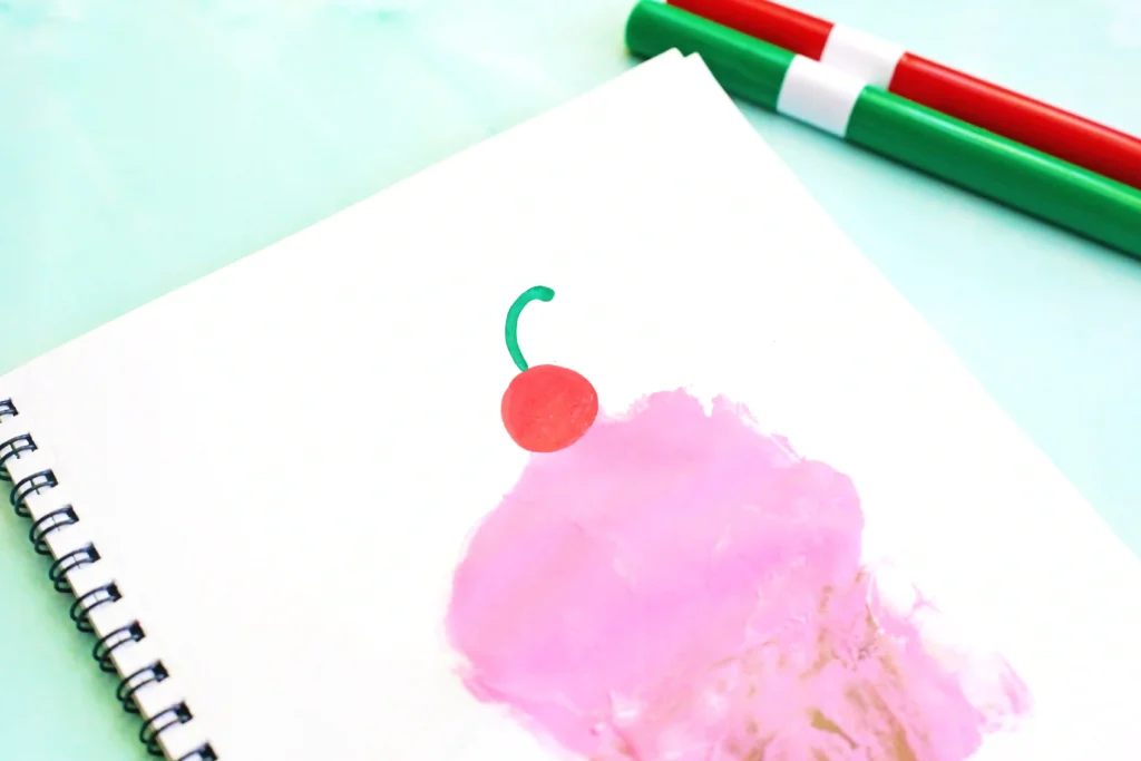 a spiral notebook with a drawn ice cream cone with a pink handprint and a cherry to look like an ice cream cone