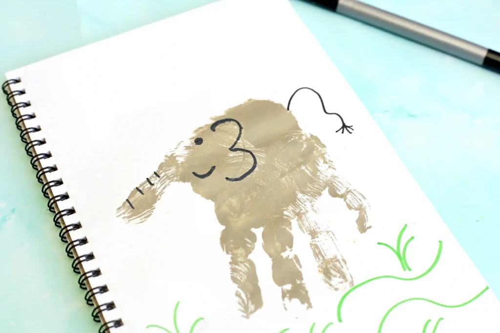 Letter E Elephant Handprint Craft - Cultivating Brilliant Minds a child's handprint in gray on a notebook designed to look like an elephant for this alphabet craft