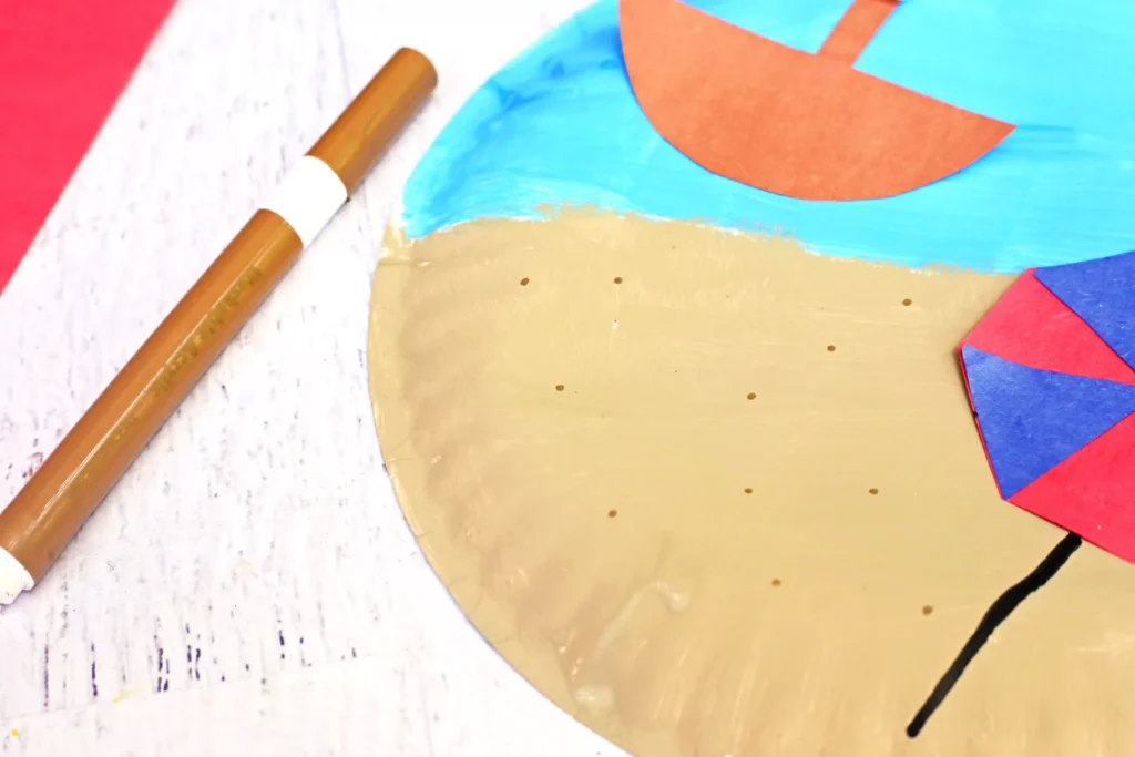Brown marker resting on a white wooden surface beside colorful abstract paper shapes in blue, orange, red and gold.