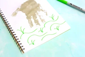 Spiral notebook open to a page with a beige handprint and bright green decorative swirls on a pale blue surface, with a green pen nearby.