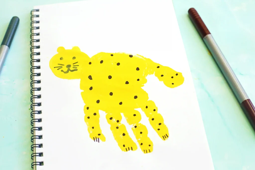 Bright yellow jaguar illustration on a white spiral notebook page with markers on a pale blue desk edge for this animal craft for kids