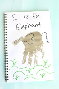 Notebook page with handwritten 'E is for Elephant' and a brown elephant stamp/paint, surrounded by green vine doodles.