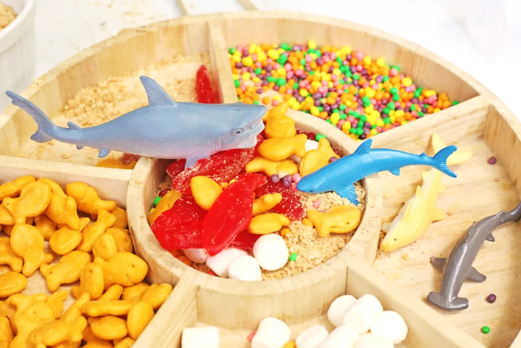 Blue shark-shaped toy rests on a display of colorful candies in wooden crates.
