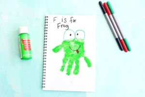 a letter f handprint craft that is a green handprint decorated to look like a frog