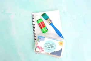 supplies for this frog craft for kids: paper, paintbrush, green paint, and markers