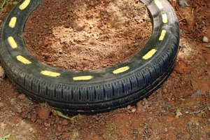 Old tire filled with reddish-brown soil on bare ground, yellow paint marks along the rim edge.