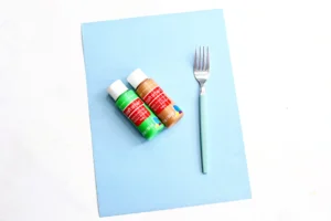 supplies for this summer craft for kids - a blue piece of construction paper, a fork, and green and brown paint
