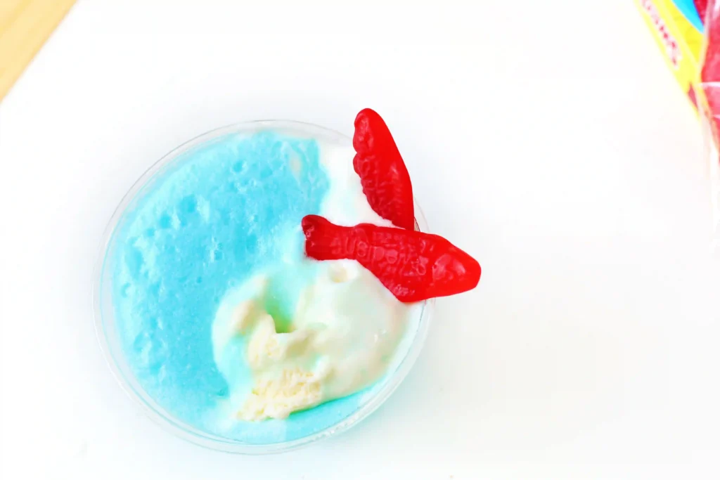 Blue and white swirled ice cream in a clear cup topped with a red gummy hand candy on the edge of the cup.