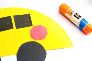 Close-up of a craft project: yellow semicircle paper plate with black shapes and a red hexagon to look like a school bus