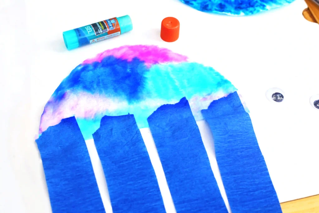 Coffee Filter Jellyfish Craft - Cultivating Brilliant Minds a tie dye colored coffee filter with blue streamers glued on