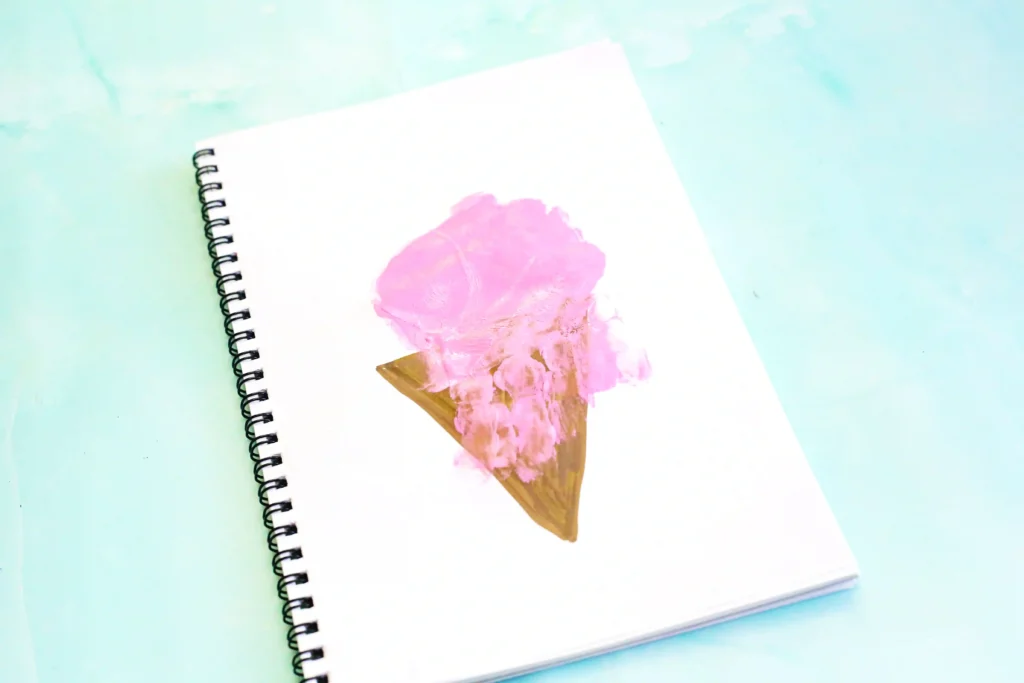 White spiral notebook with a pink paint handprint on a brown triangle to look like an ice cream cone