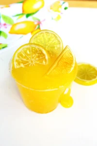 Tall glass of a lemon slime recipe with lemon slices and a lemon wedge, set against a bright background with citrus decor.