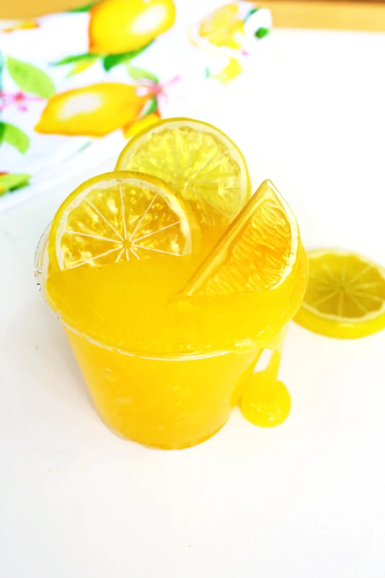 Tall glass of a lemon slime recipe with lemon slices and a lemon wedge, set against a bright background with citrus decor.
