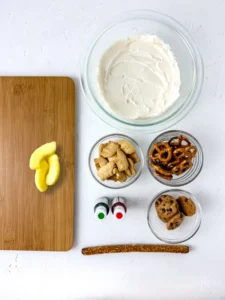 ingredients for this back to school treat - wooden board, buttercream, red and green food dye, pretzels, cookies, apple slices