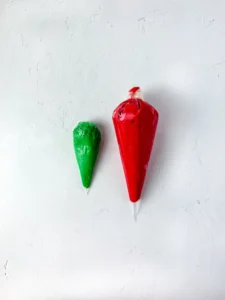 Two piping bags filled with red and green icing on a pale textured surface, ready for decorating for this back to school treat