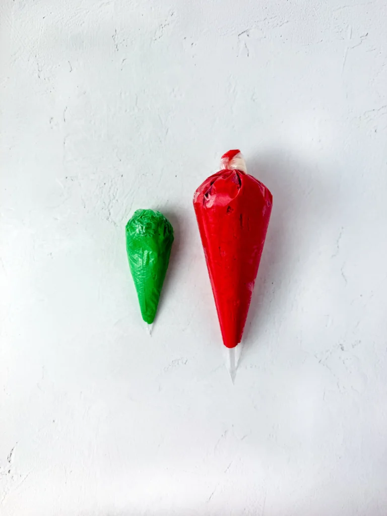 Two piping bags filled with red and green icing on a pale textured surface, ready for decorating for this back to school treat
