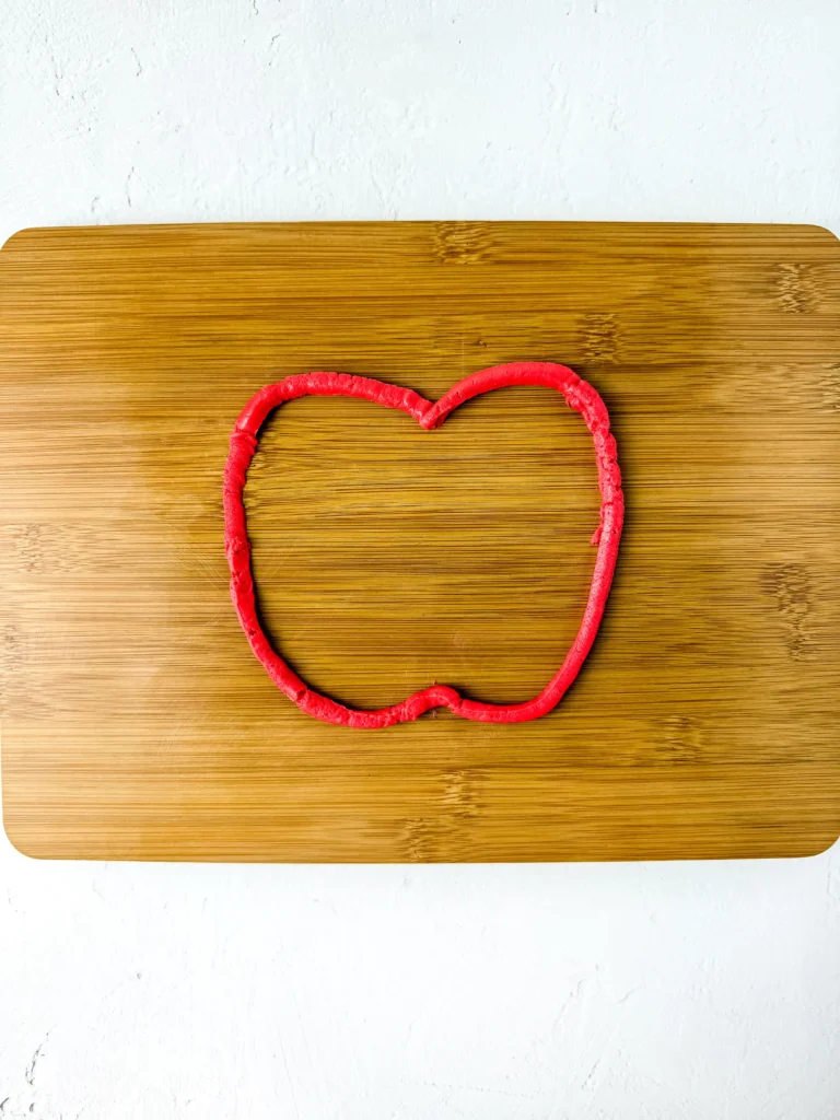 Red apple-shaped outline made of red buttercream on a wooden table surface for this back to school snack