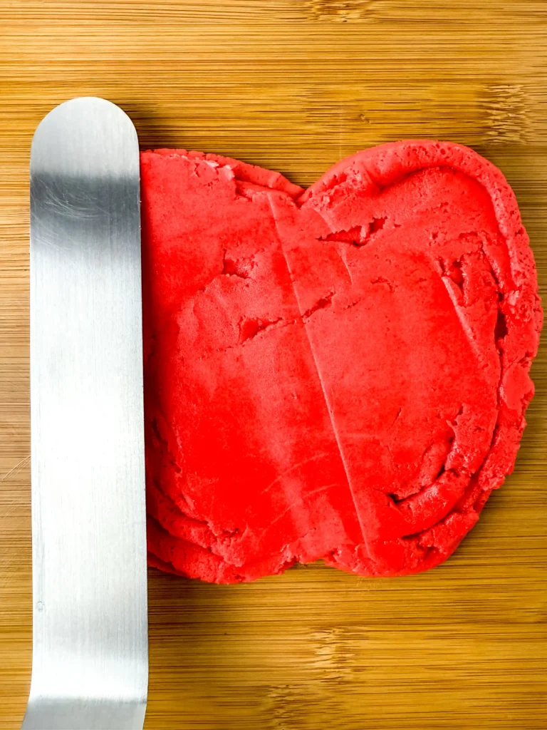 Red buttercream shaped into an apple with a stainless steel spatula resting on a wooden surface on top of a cutting board for this party dessert board
