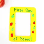 a First Day of School Photo Frame that is painted yellow with fingerprint apples and words that read "first day of school"