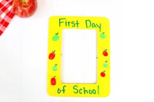 a First Day of School Photo Frame that is painted yellow with fingerprint apples and words that read "first day of school"