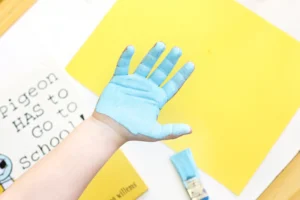 Hand covered in blue paint raised against a bright yellow background in an art setup.