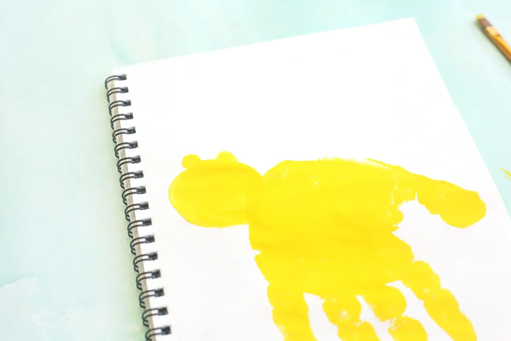 Spiral-bound notebook page with a large yellow paint smear on white paper atop a pale blue surface for this alphabet craft for kids