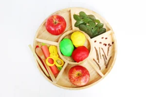 supplies for the parts of an apple playdough tray - whole apple, leaves, sticks, playdough, and apple seeds