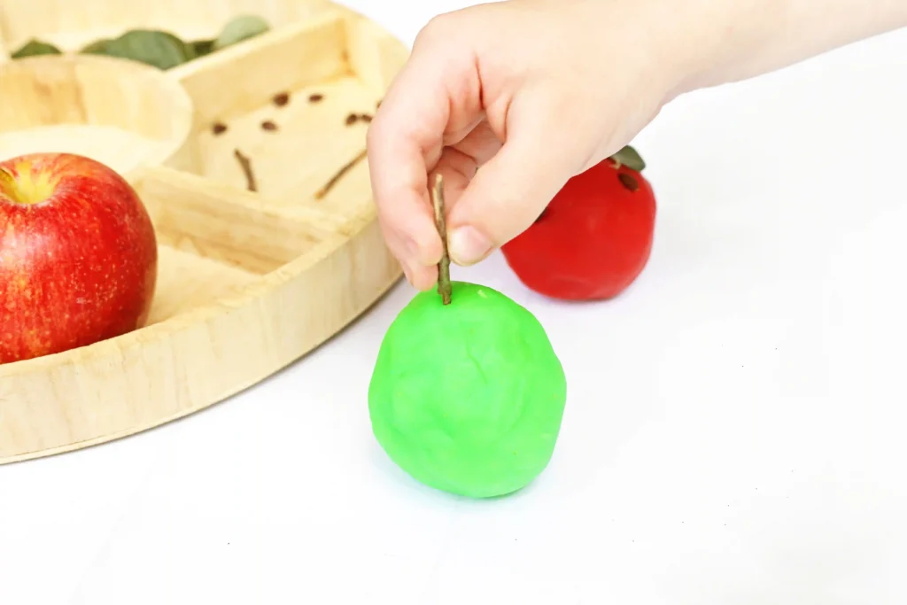 Hand putting a stick into a green playdough apple