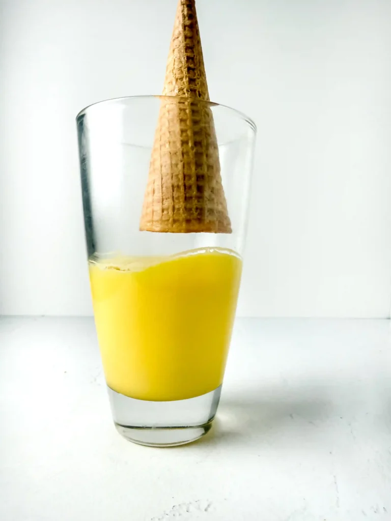 Glass of bright yellow candy melts with a tall wafer cone standing upright inside the rim for this back to school snack
