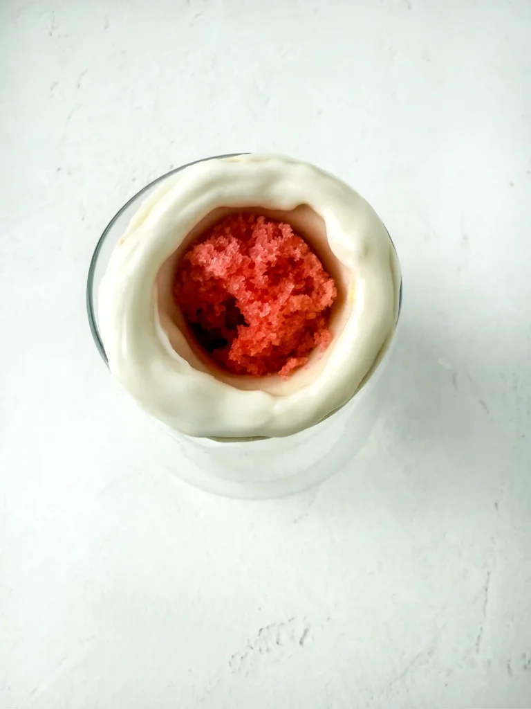 Top-down view of a glass dessert with a white creamy outer layer and a red crumb filling in the center for these pencil cupcakes