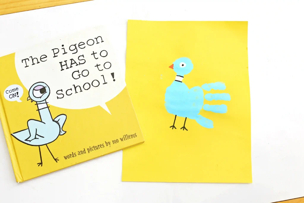 a pigeon handprint craft that is a blue handprint on yellow paper with details to look like a pigeon next to the book "The pigeon has to go to school"