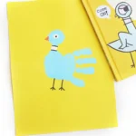 a pigeon handprint craft that is a blue handprint on yellow paper with details to look like a pigeon next to the book "The pigeon has to go to school"