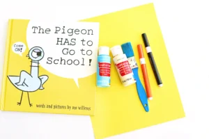 supplies for this mo willems craft - yellow construction paper, blue and white paint, black and orange markers, a paintbrush, and the book "The Pigeon HAS To Go To School"