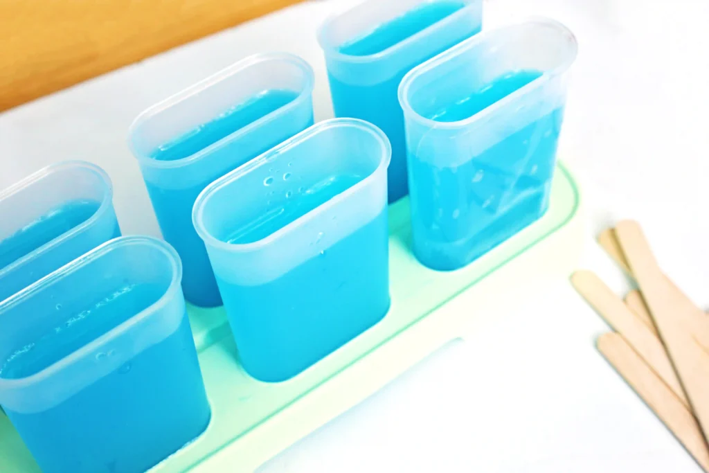 Blue liquid in clear popsicle molds held in a plastic rack for this easy summer dessert