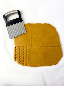Orange-brown rolled-out cookie dough on a white surface with a crinkle cutter nearby, ready to cut shapes.