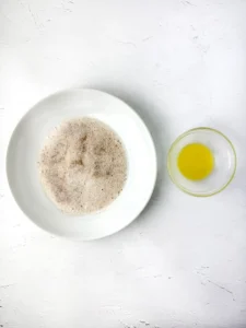 White plate piled with brown sugar beside a small glass bowl holding a melted butter on a white textured surface.