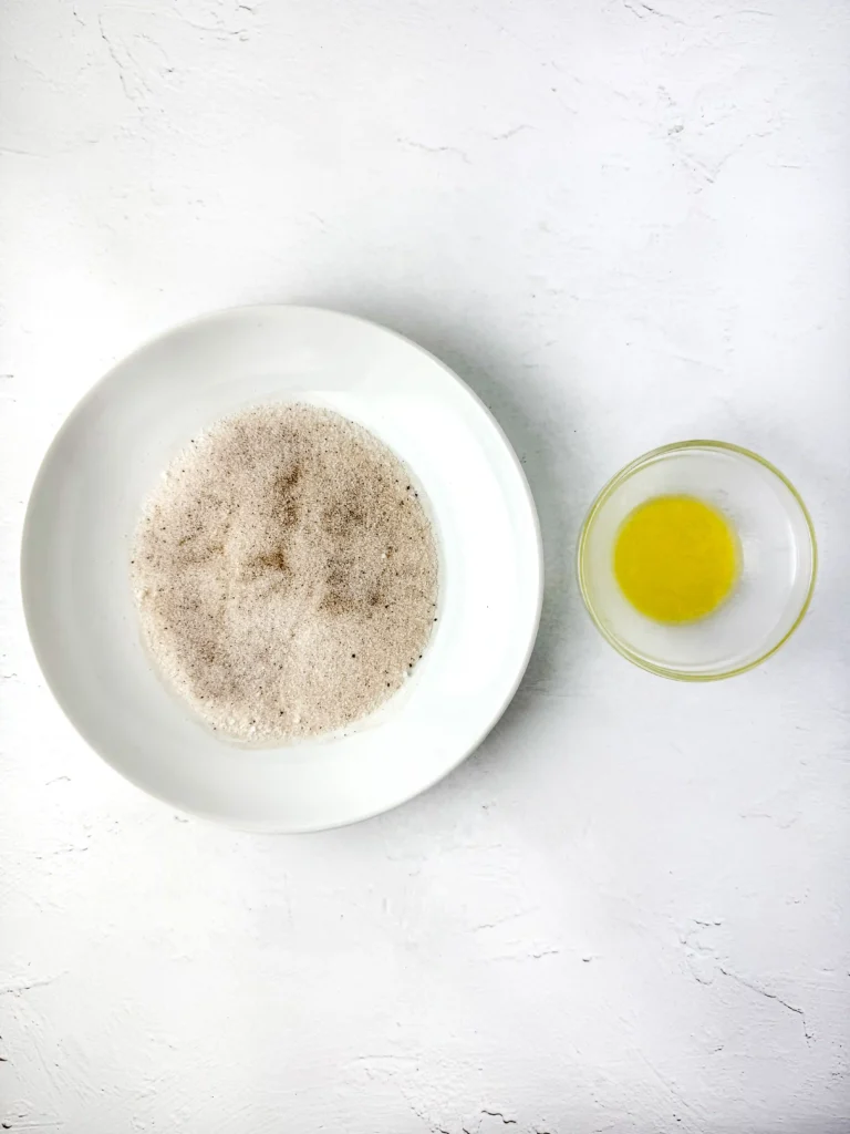White plate piled with brown sugar beside a small glass bowl holding a melted butter on a white textured surface.