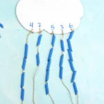 a Raindrop Counting Activity that is a cardboard cloud with blue dyed pasta strung on
