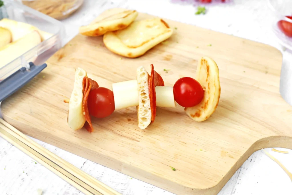 Skewered bite-sized sandwiches with bread, slices of pepperoni, cheese, and a cherry tomato on a wooden board for this backyard picnic idea