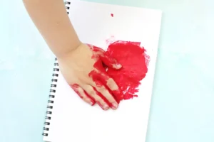 a child stamping his red painted hand down a notebook for this heart craft