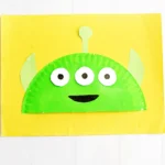 a Toy Story Alien Paper Plate Craft that is a paper plate cut in half, painted green, and decorated to look like the alien from toy story