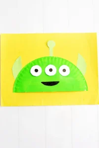 a Toy Story Alien Paper Plate Craft that is a paper plate cut in half, painted green, and decorated to look like the alien from toy story