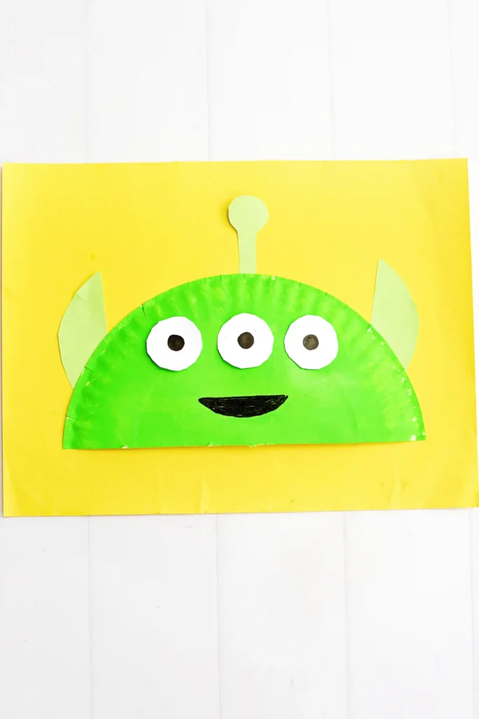 a Toy Story Alien Paper Plate Craft that is a paper plate cut in half, painted green, and decorated to look like the alien from toy story