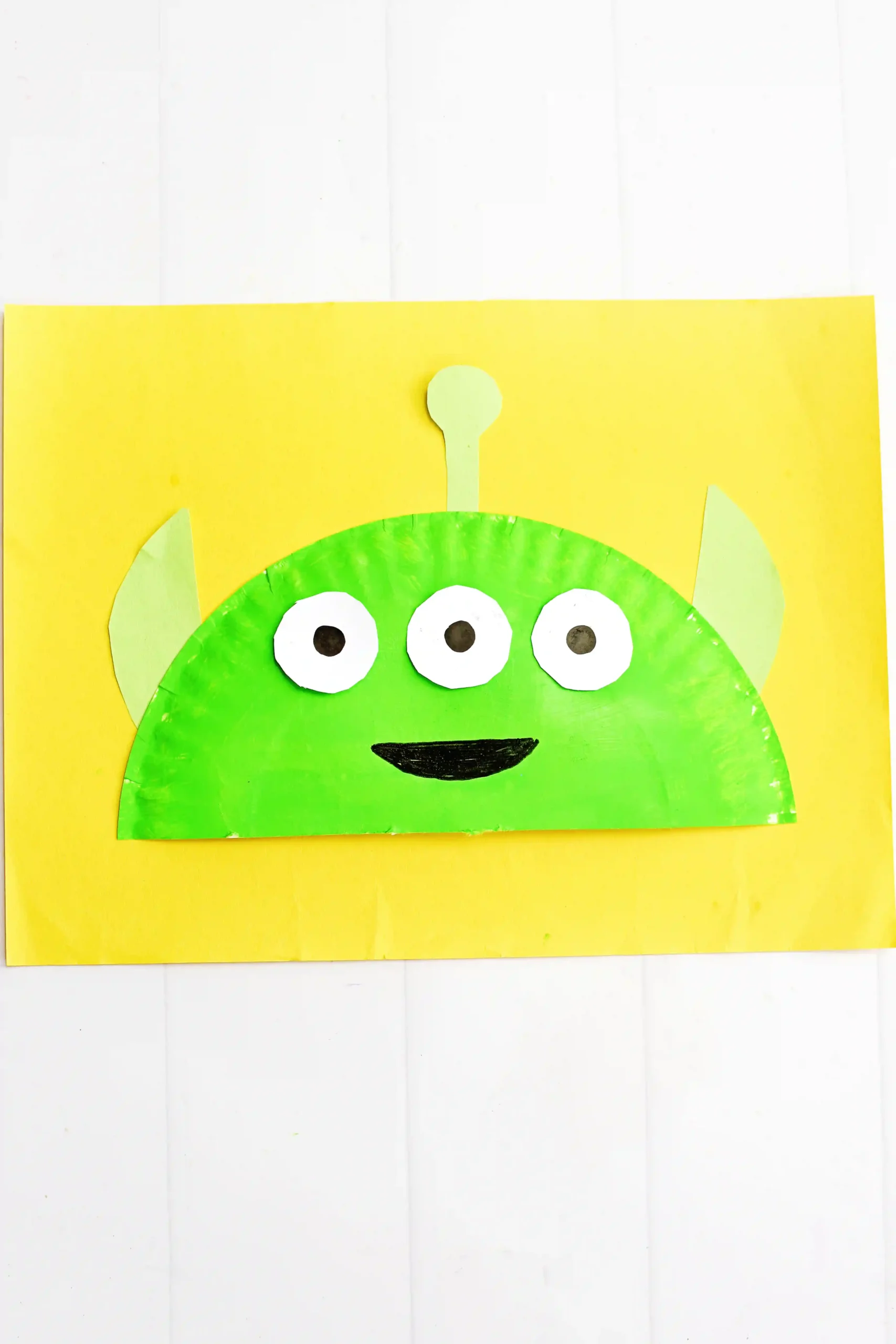 a Toy Story Alien Paper Plate Craft that is a paper plate cut in half, painted green, and decorated to look like the alien from toy story