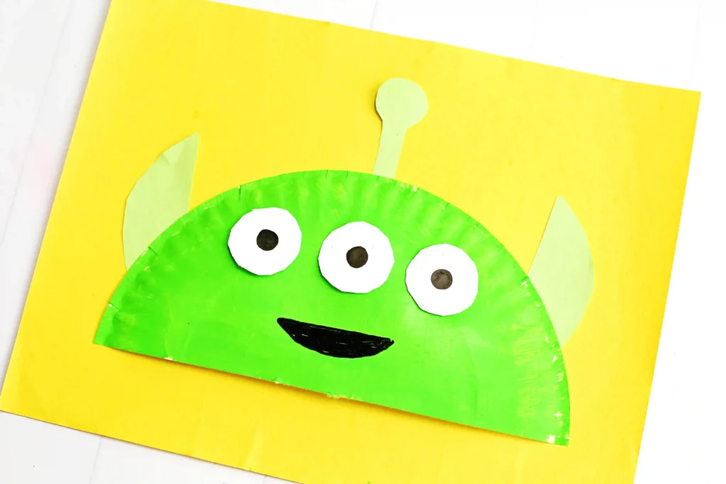 a Toy Story Alien Paper Plate Craft that is a paper plate cut in half, painted green, and decorated to look like the alien from toy story