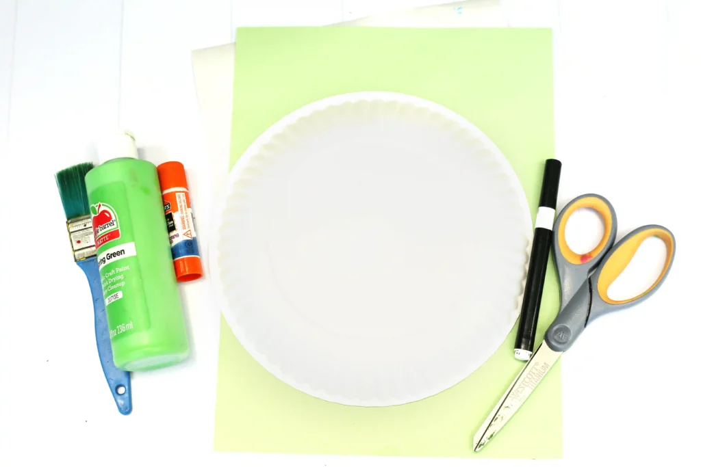 supplies for the toy story craft: glue bottle, paint, brushes, scissors, ruler, and a white paper plate center stage.