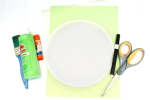 supplies for the toy story craft: glue bottle, paint, brushes, scissors, ruler, and a white paper plate center stage.